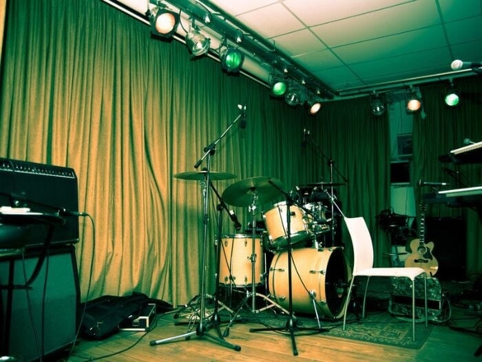 Empty stage with drum kit, cast in green light in a small music venue.