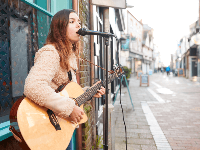 Female musician busking, playing acoustic guitar and singing outdoors in the street.