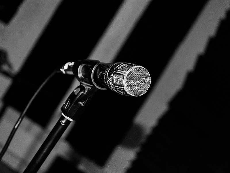 Photograph of a microphone stood against a fairly plain background, in black and white.
