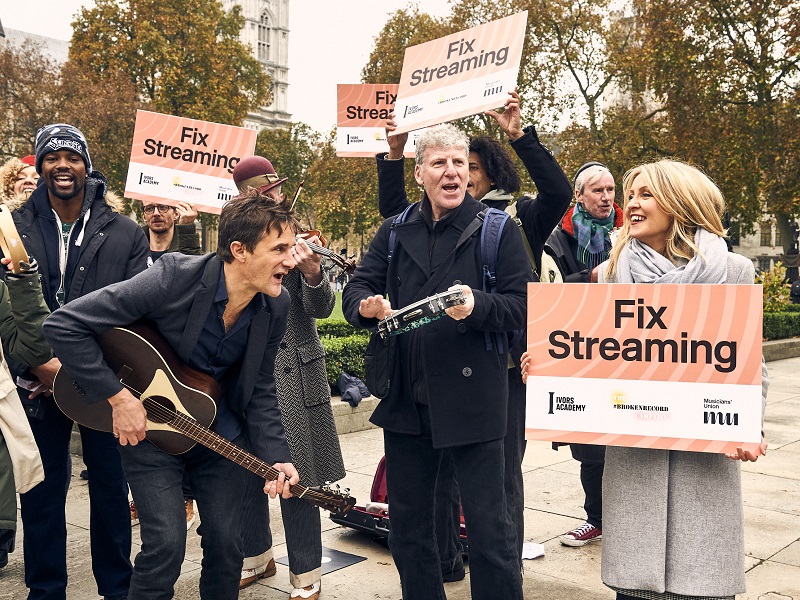 Esther McVey and a crowd of musicians with protest signs saying 'fix streaming' outside of parliament for the 2021 campaign demo.