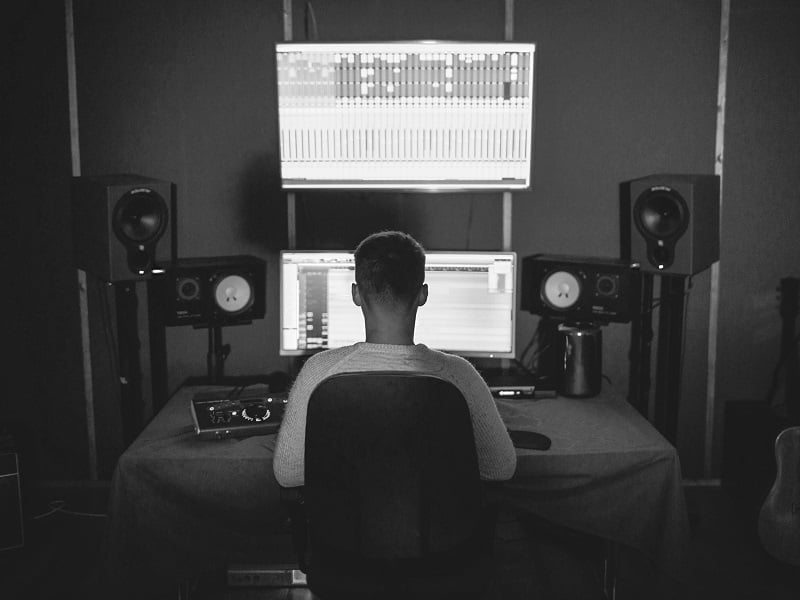 Photograph of a person at a mixing desk, we're looking at the from behind so just see the back of their head, and the two screens stacked up in front of them.
