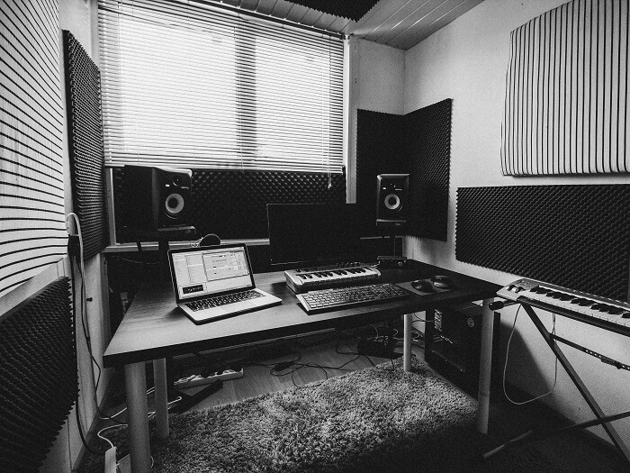 Inside of a home music studio, with open laptop and small midi keyboard on desk, and sound proofing around the room.