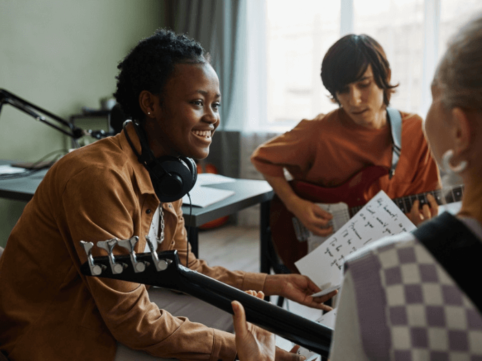 Three young musicians, sat smiling in a circle working together playing guitar.