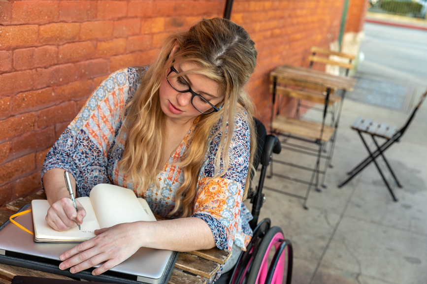 Young woman studying with a notebook in a wheelchair