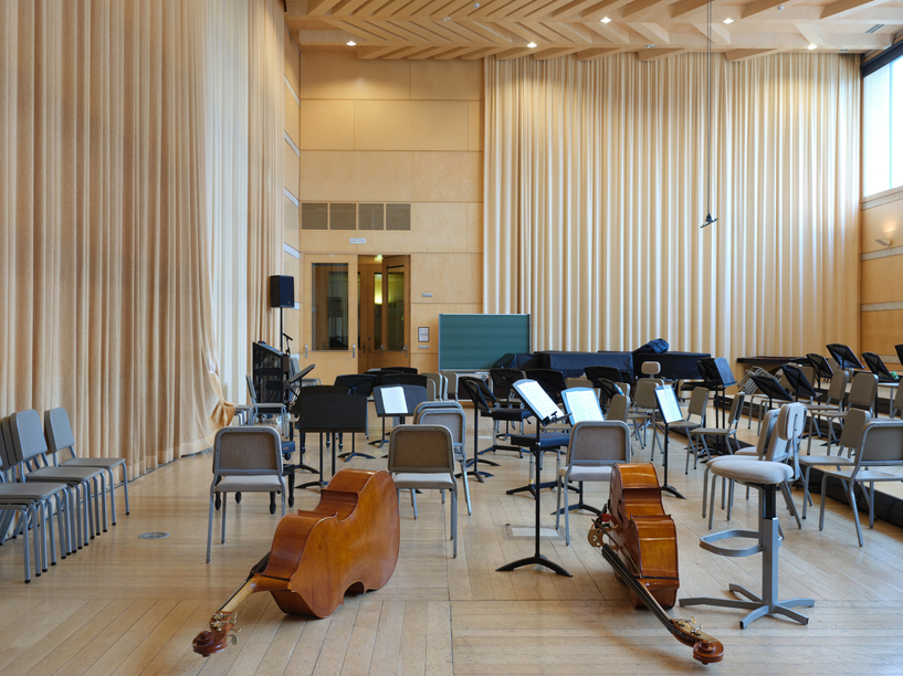 Photograph of an empty recital hall, there are two double basses lying on their sides and a lot of empty chairs and music stands.
