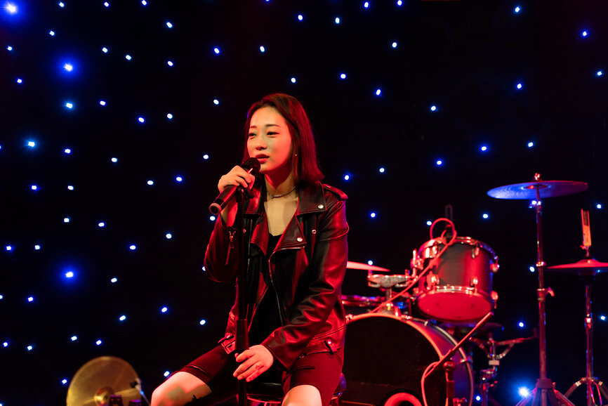 young female musician on stage with a microphone, with drums in the background