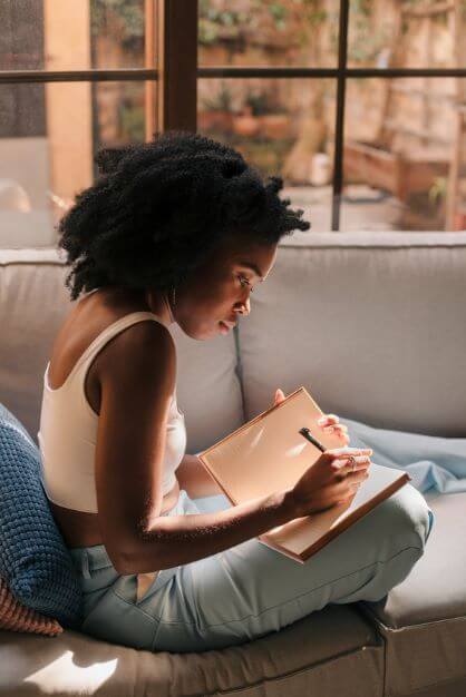 young black woman on a sofa making notes in her notebook
