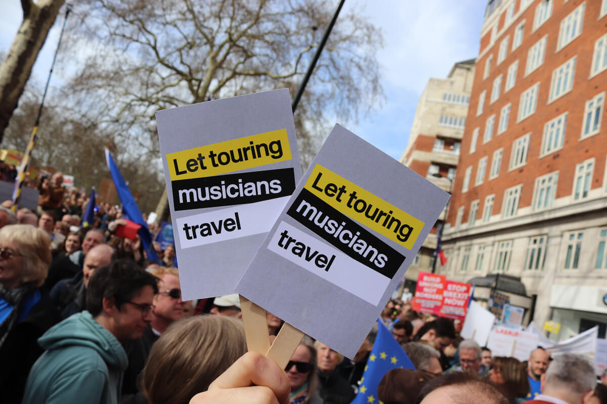 Someone holding the 'Let touring musicians travel' placards in the crowd