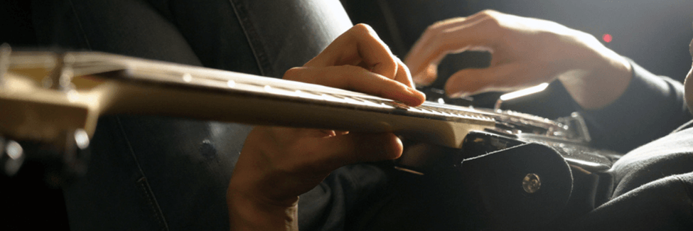Close up of someone playing guitar, their hands both on the fretboard.