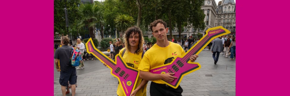 Marcelo and another busker in yellow M U campaign t-shirts holding pink cut out guitars at a demo last August.