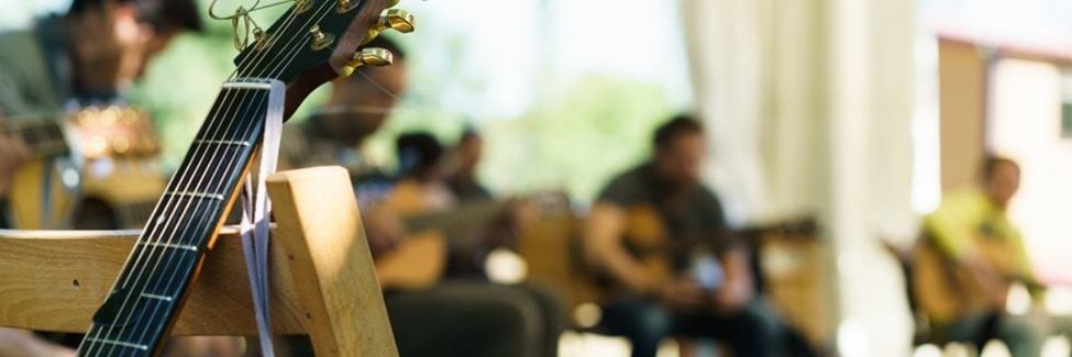 Out of focus interior of a school music classroom, with students practicing musical instruments and an acoustic guitar in the foreground.