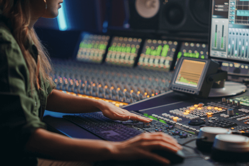 A female at a mixing desk in a recording studio.