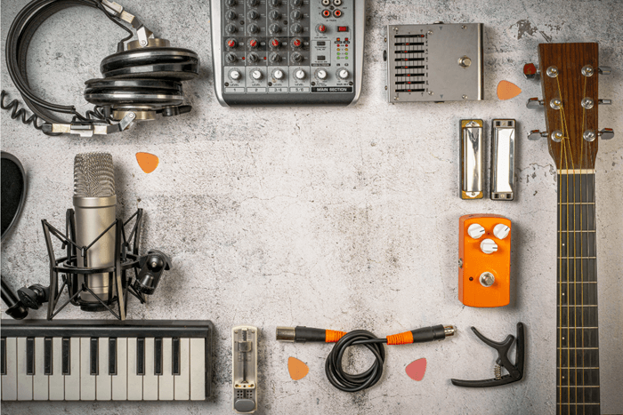 Flat lay of musician and sound engineer items such as a guitar, mixer, microphone, keyboard, cables, note pad and headphones. Image has a vintage style filter.