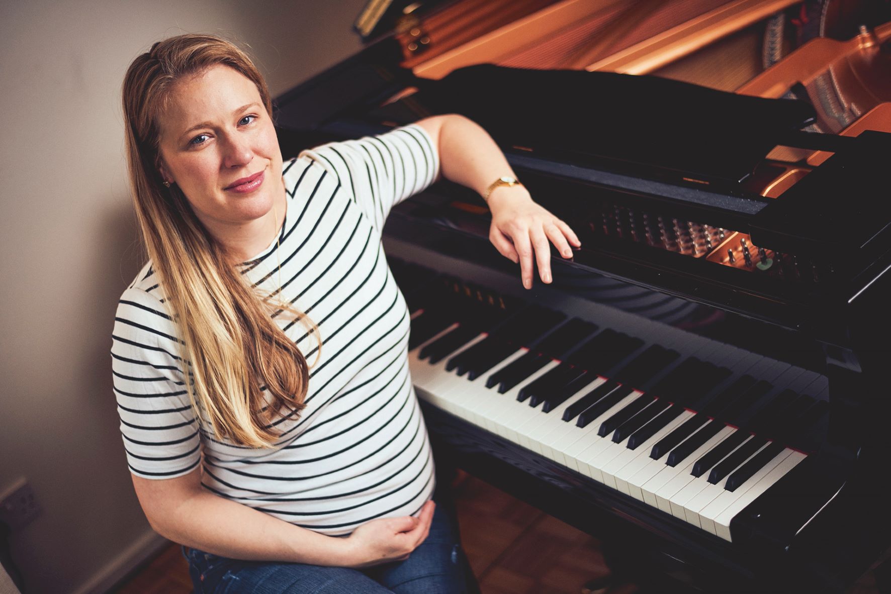 Pregnant Jocelyn Freeman sits, one hand on her baby bump, another on a piano.
