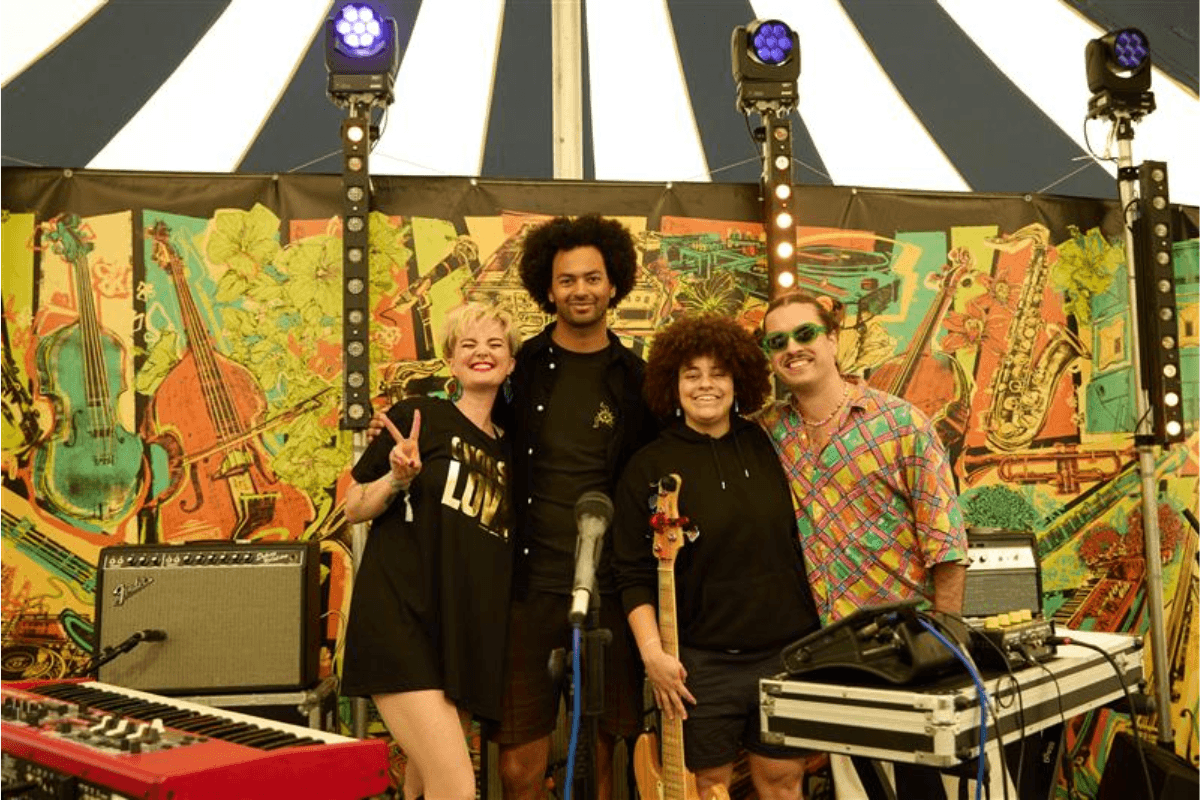 The band members of 10:32 standing on a festival stage and smiling as they pose for a photo.