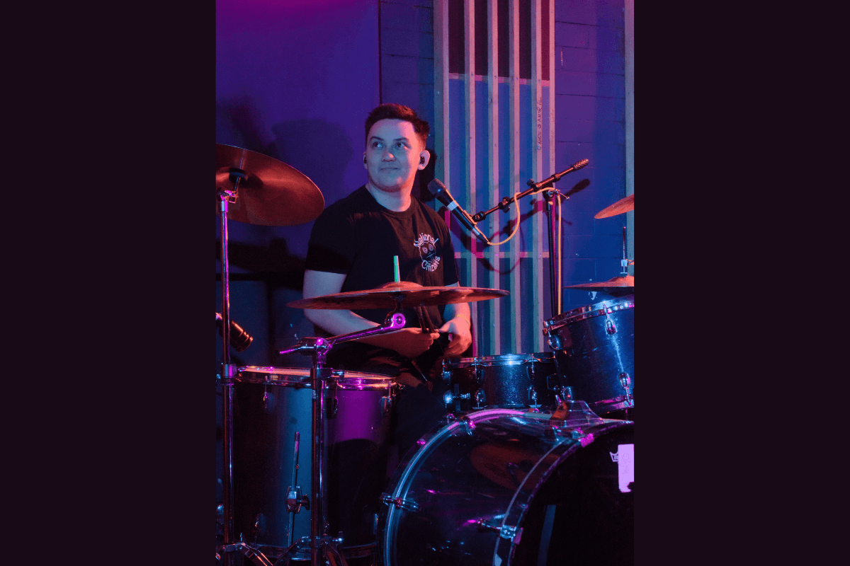 Asher playing the drums in a room lit by purple lights.