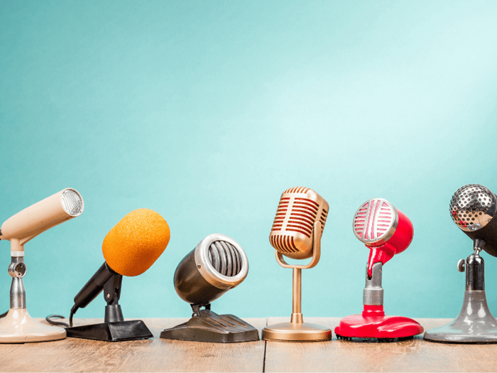 Collection of 6 retro style microphones on a desk with a sky blue back drop.