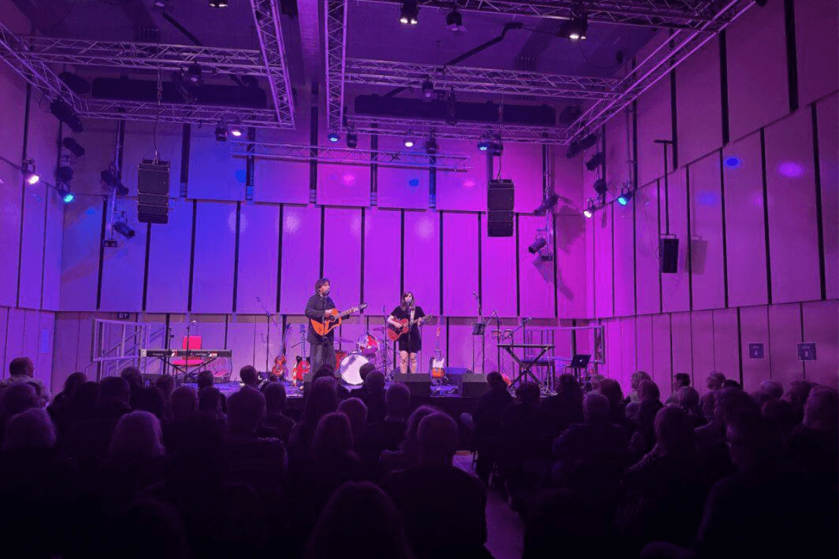 Roxanne performing on stage with another musician in front of a small crowd, the stage is lit in purple lighting.