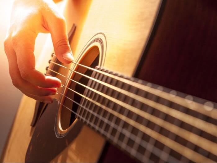 Close up of hand plucking strings on an acoustic guitar.