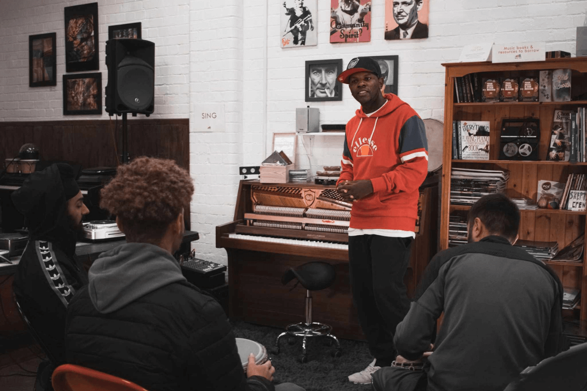 Xidus speaking to a group of young men in a music room.