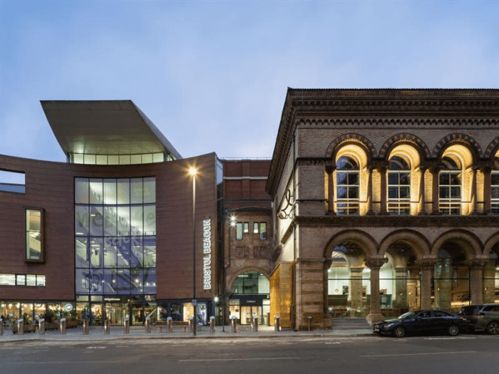 The exterior street view of the Bristol Beacon, a large modern venue next to some older buildings.