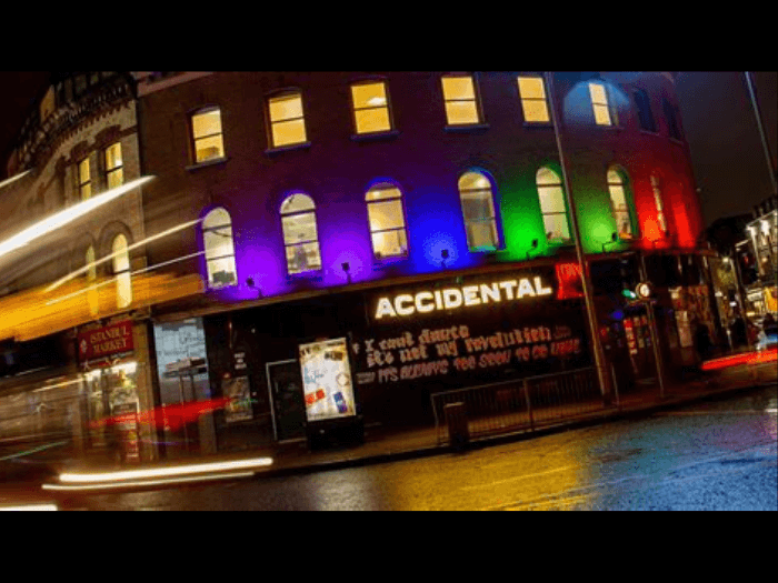 Street view of the venue at night time, the signage is lit up by rainbow lights.