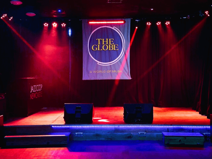 Venue stage with low lighting and a banner saying 'The Globe'.