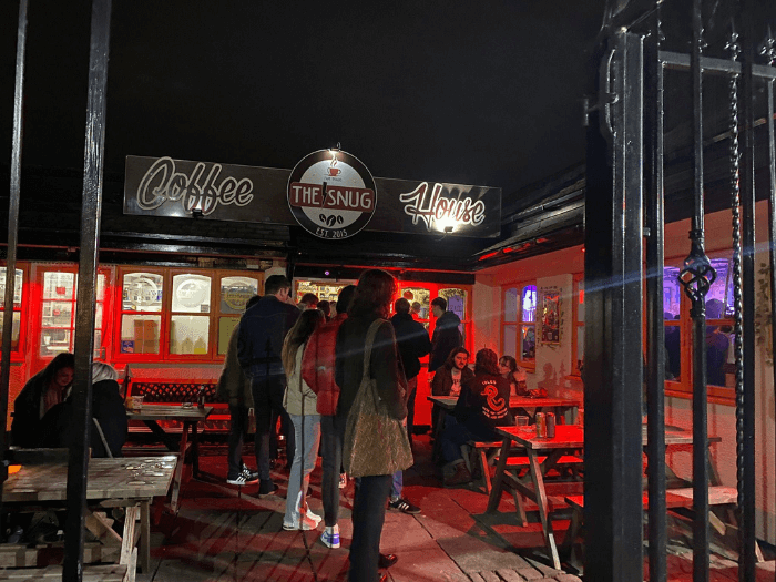 Outside of the venue in the evening, people are sat outside with a drink and queuing to get in.