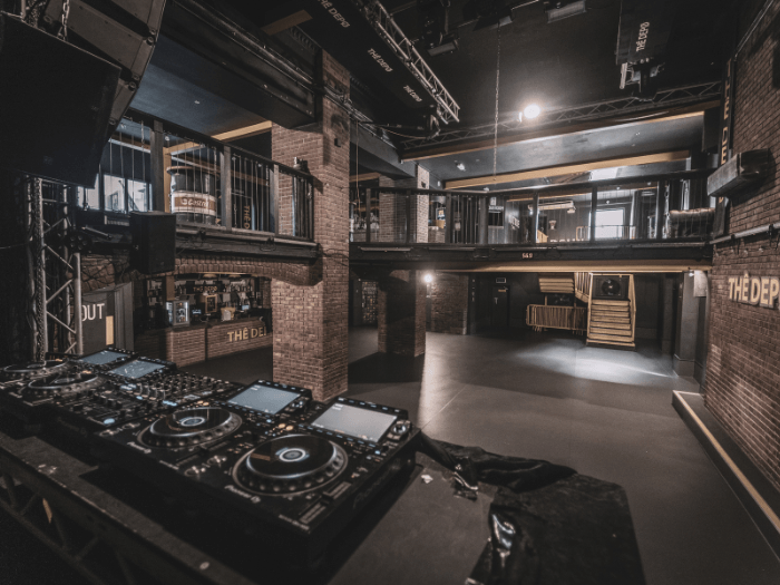 Inside of the basement venue, showing two levels, exposed brick and a some DJ decks.