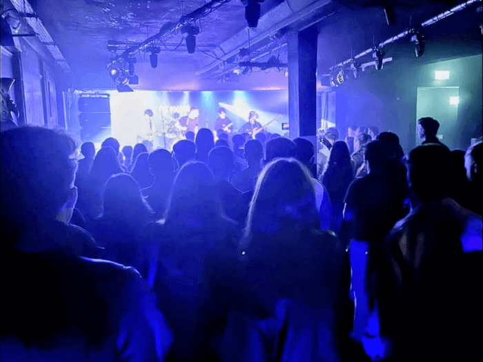 Inside of the venue. A crowd watching a band on stage with blue light on them.