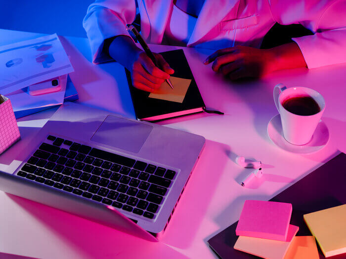 A person sitting at a desk and writing on a sticky note with a laptop open.