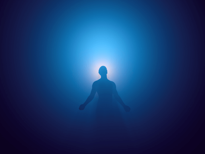 Black background with blue light illuminating the silhouette of a man with his arms outstretched, representing ascension meditation