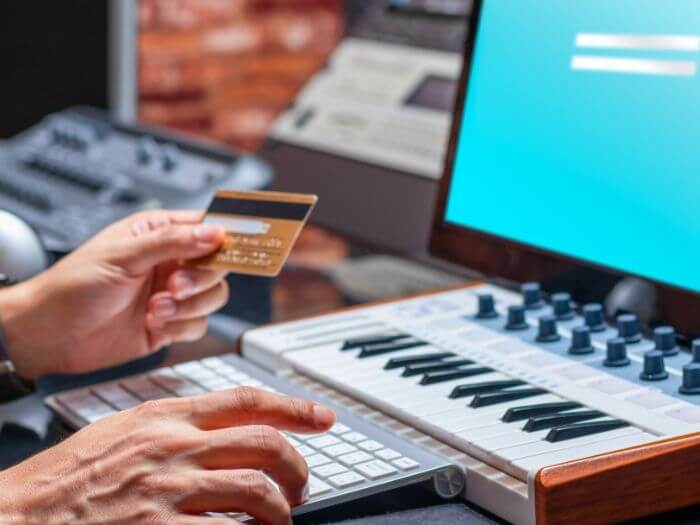 Hand holding a credit card in front of midi keyboard and computer.