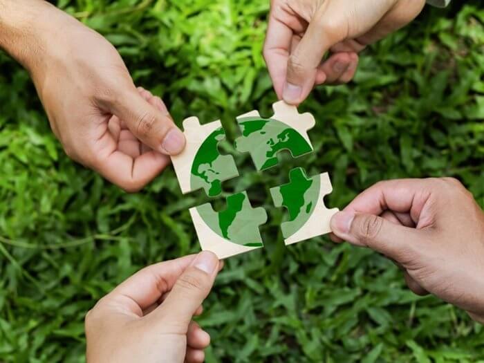Close up of four hands holding a piece of jigsaw that come together to make a green globe.