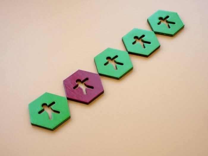 A row of green wooden hexagons with figures in, a red one in the middle represents the concept of Impostor Syndrome.