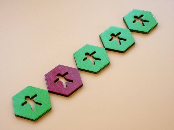 A chain of wooden hexagons, with people cut out in the centre. They are all green apart from one which is red, representing imposter syndrome.