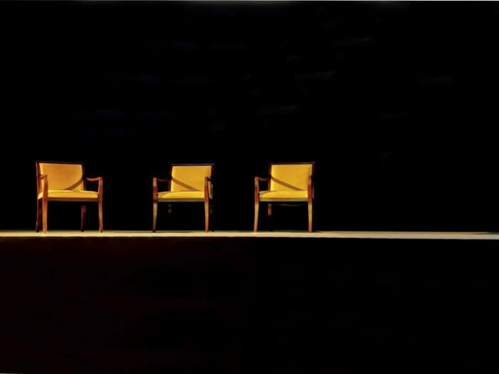 Three empty, yellow, wooden chairs on a stage with black background.