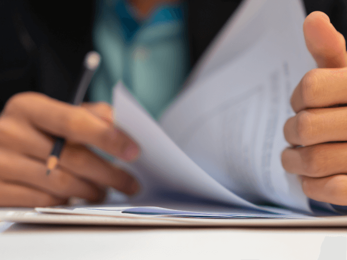 Close up of hands flicking through contracts/legal paper work, while holding a pencil ready to make notes.