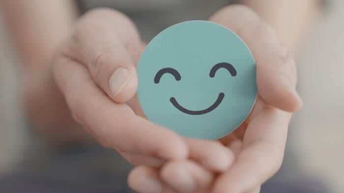 Two hands holding a green smiley face to represent mental health.