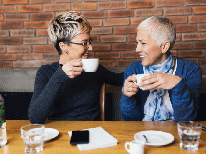 Two women sat smiling and drinking coffee at a table.