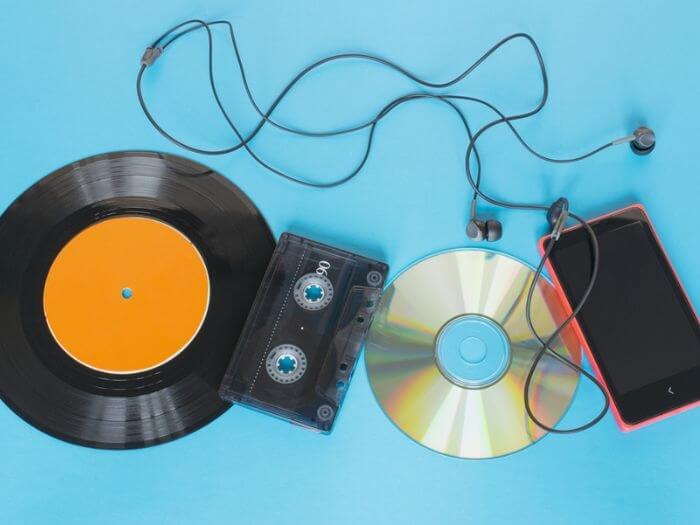 Evolution of music platform concept, showing a vinyl record, tape, disk and smartphone with headphones, on a blue background.