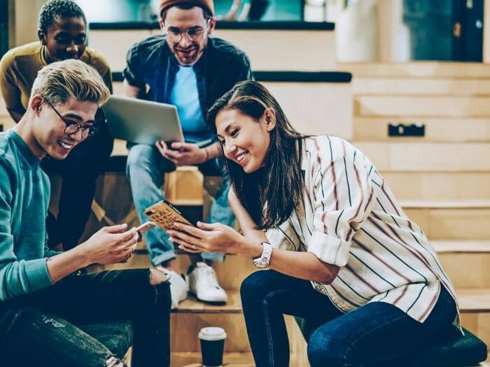 Group of people smiling, drinking coffee and sharing things on their phones.