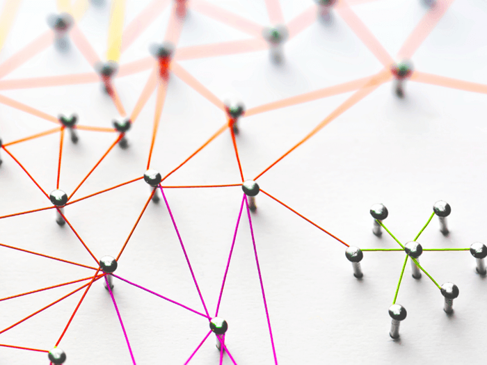 Pins stuck into a white coloured board, they are all conntected to each other by different coloured string.