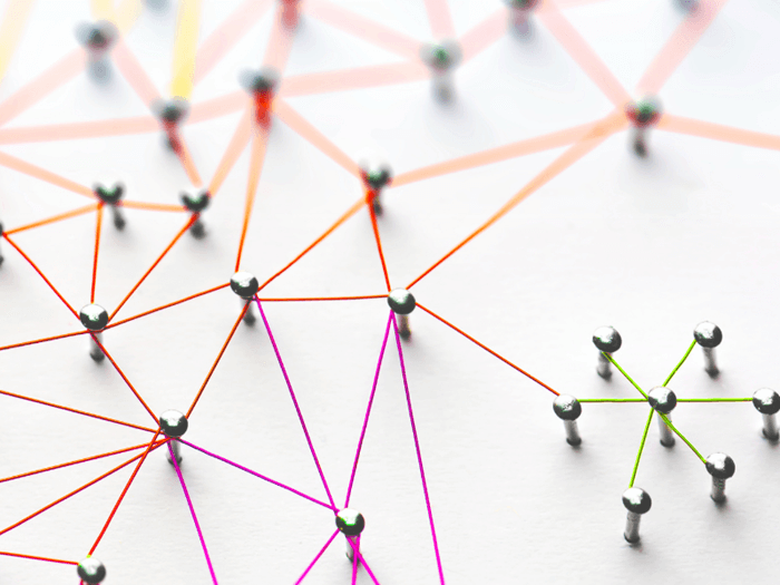 Various coloured threads crisscrossing and connected by pins on a white background, representing networking.