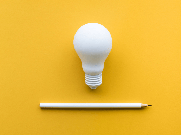 Lightbulb and white pencil on pastel yellow coloured background. Flat lay design.