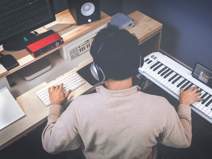 Person sat in front of a computer screen with electronic keyboard, home studio set up.