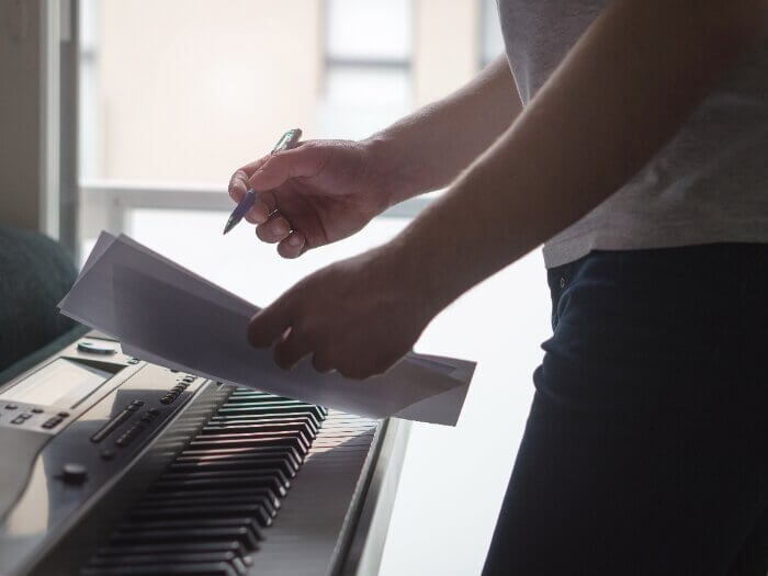Person in shadow holding a pen and paper over a keyboard.