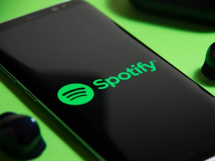 Close up of black smart phone with the Spotify logo on, next to black earbud headphones.