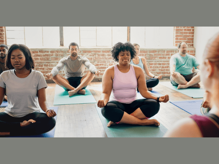 Diverse group of men and women sat on the floor on yoga mats in a studio.