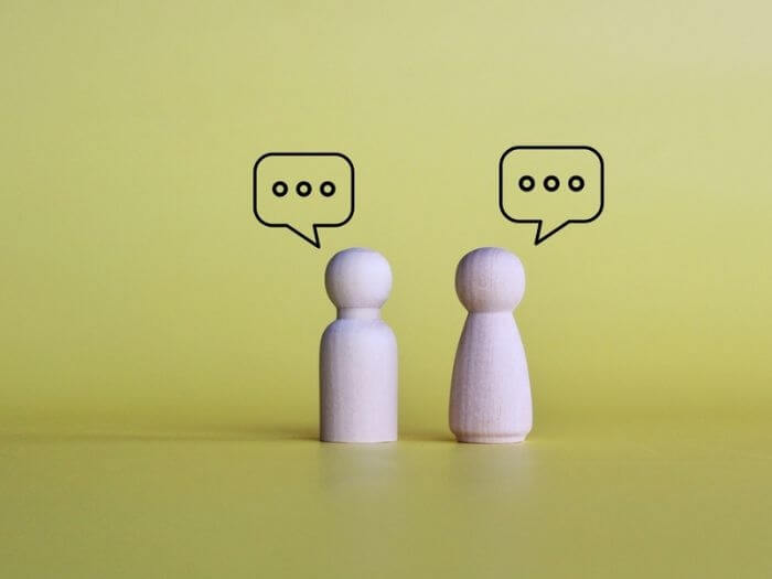 Wooden dolls chatting with speech bubbles on a yellow background. Social interaction and chat concept.